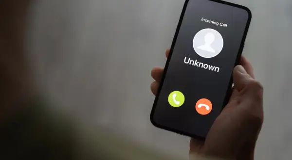 Dłoń trzyma smartfon z ekranem pokazującym przychodzące połączenie od nieznanego numeru. Czy to kolejny **wangiri**?