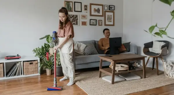 Kobieta sprząta mieszkanie odkurzaczem Dyson, podczas gdy mężczyzna pracuje na laptopie. Zastanawiasz się, który Dyson wybrać?