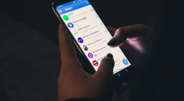 Dłonie trzymają smartfon z otwartą aplikacją Telegram. Czy telegram jest bezpieczny? Aplikacja wyświetla listę czatów i kanałów.