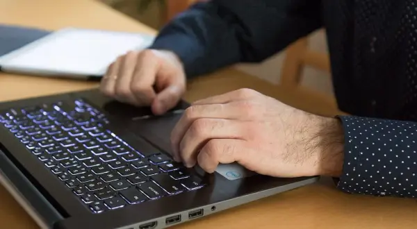 Dłonie pracują na podświetlanej klawiaturze laptopa, korzystając z funkcji biometrii do logowania.