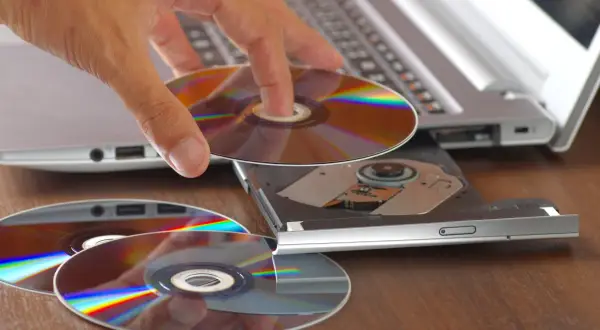 Dłoń wkłada płytę CD do napędu laptopa. Program cdburnerxp pomoże nagrać dane.