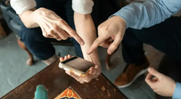 Dwie osoby wskazują palcami na ekran telefonu, dyskutując, ile kosztuje aplikacja.