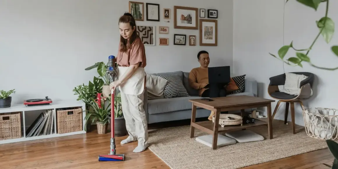 Kobieta sprząta mieszkanie odkurzaczem Dyson, podczas gdy mężczyzna pracuje na laptopie. Zastanawiasz się, który Dyson wybrać?