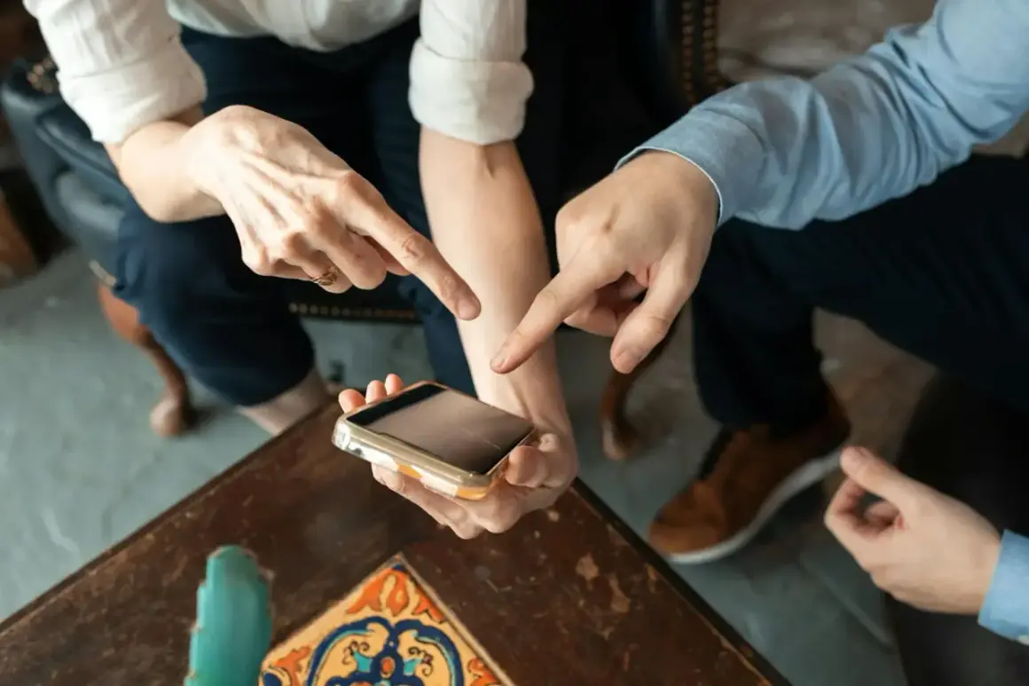 Dwie osoby wskazują palcami na ekran telefonu, dyskutując, ile kosztuje aplikacja.